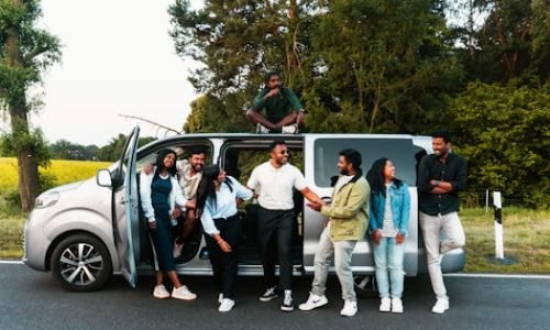 A group of friends having fun by a van on a scenic road trip in nature.