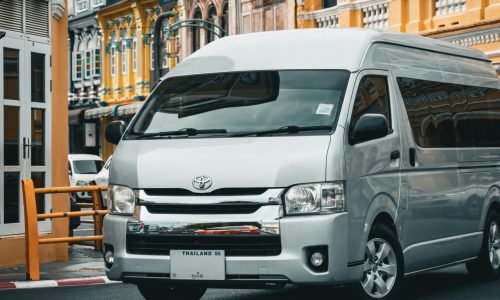 A modern van in front of colorful colonial buildings on a street in Phuket, Thailand.